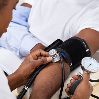 A Black woman health professional takes a Black man’s blood pressure