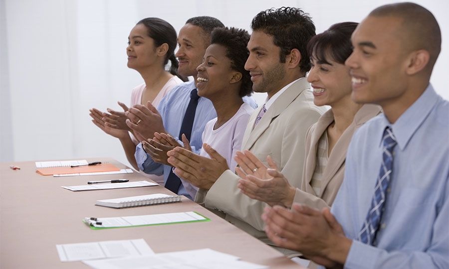 A diverse group clapping hands around a conference table.