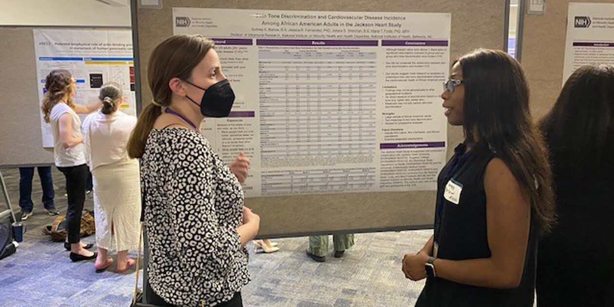 NIMHD postbac Sydney Barlow discusses her research on skin tone discrimination in health care with an attendee at the 2023 Postbac Poster Day