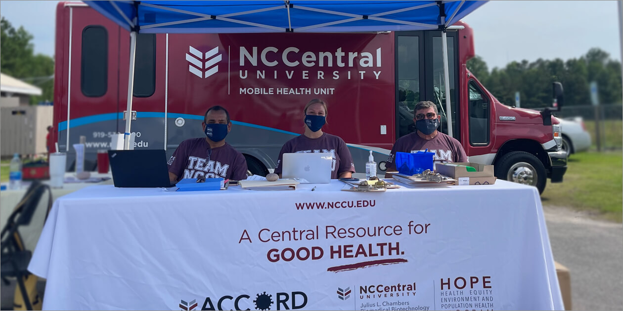 Three NCCU team members staff an ACCORD mobile research vehicle at an outdoor event.