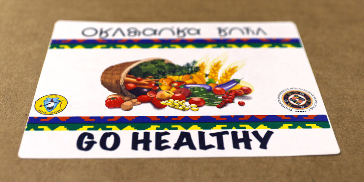 Sticker on an Osage community supported agriculture program box that says Go Healthy in Osage and English with a cornucopia graphic