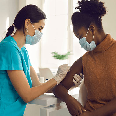 An Asian female nurse preps a Black woman to receive a COVID-19 vaccine