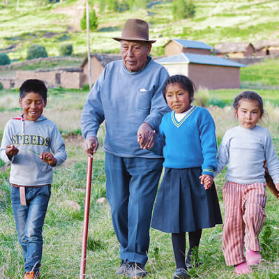 A Native American man using a walking stick walks with his 3 grandchildren in the countryside.
