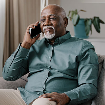 A Black older man sitting on a couch and holding a cell phone to his right ear