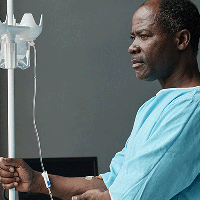 An older Black male patient holding a drip stand and staring into the distance