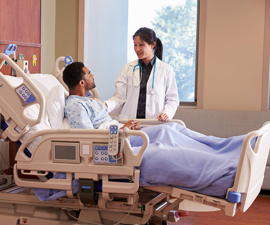 Asian, female doctor talking with a Black male patient who is in a hospital bed